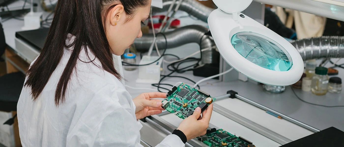 Eine Frau im Laborkittel arbeitet an einer Leiterplatte.