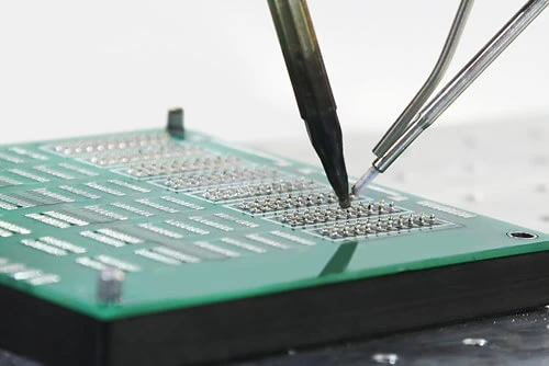 Eine Person bestückt mit einer Pinzette eine elektronische Leiterplatte.